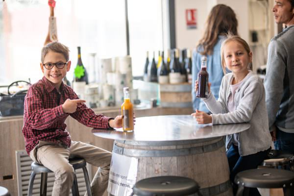 Des enfants buvant du jus de fruit assis sur une table, dans la boutique Invinaterra à Sauteyrargues