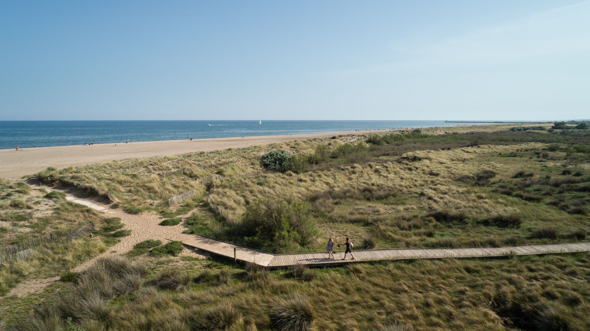 Un couple marche sur un platelage qui mène à la plage de Vendres