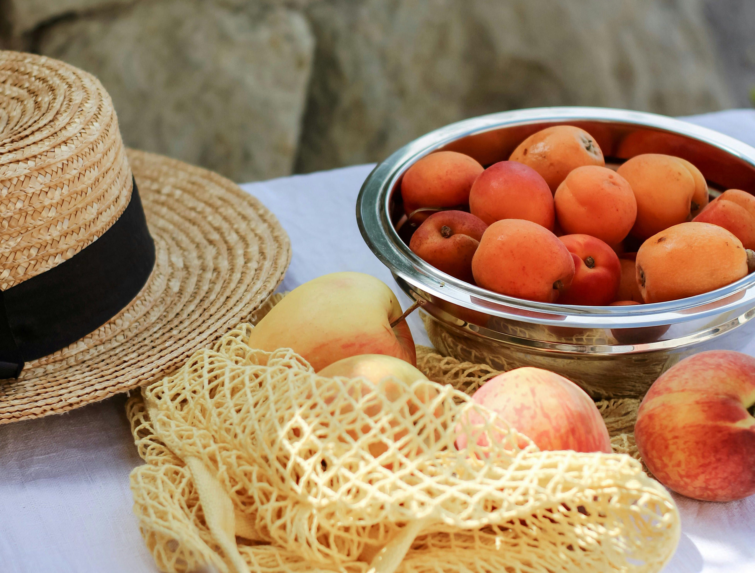 Abricots, pêches, pommes et chapeau de paille sur une table