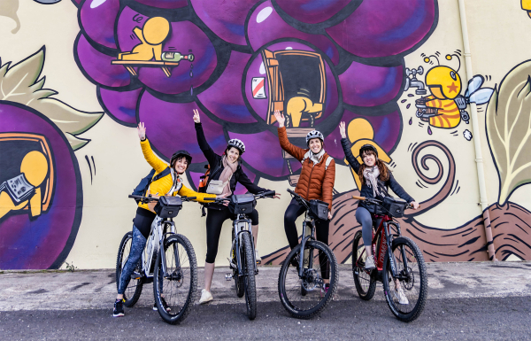 4 femmes à vélo devant une fresque géante du street-artist Jace apposée sur l'un des murs de la cave de Cazouls-lès-Béziers
