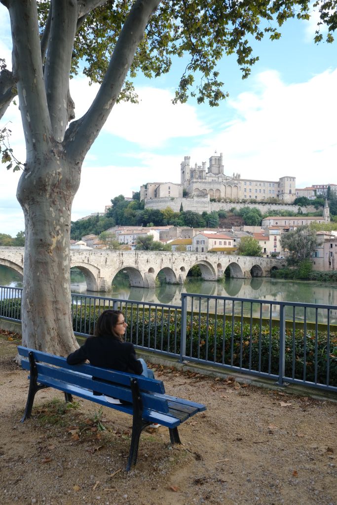 Femme assise sur un banc au bord de l'Orb face à la cathédrale saint Nazaire de Béziers et le Pont Vieux