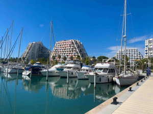 Port de la Grande Motte. Des bateaux sont amarrés avec en arrière-plan le 1ᵉʳ bâtiment construit nommé la pyramide.