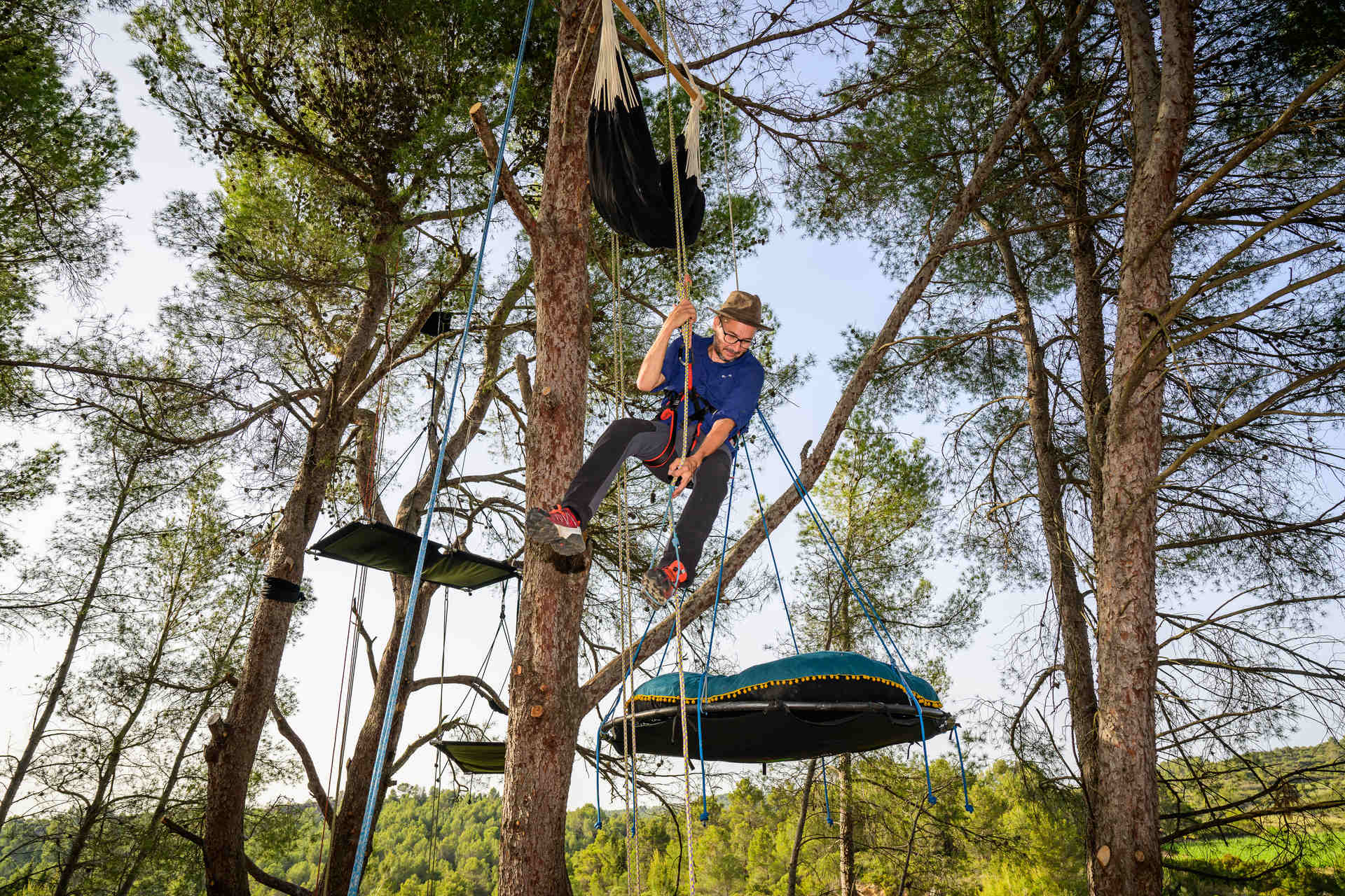 Homme qui grimpe dans un hamac dans les arbre avec l'Arbre Nomade à Oupia